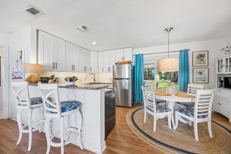 Bright, open kitchen with coastal charm where you'll find everything you need to prepare meals—stainless appliances, granite counters, island seating, and a sunny dining nook.