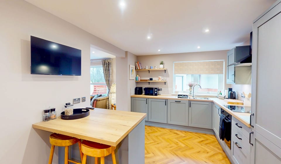 The kitchen at Kestrel Lodge features a handy breakfast bar with stools, ideal for a casual family breakfast before a day of adventure. The grey shaker units, wooden worktop and well-stocked shelving make this kitchen as practical as it is stylish, while the large wall-mounted TV adds a touch of comfort for those leisurely mornings.
