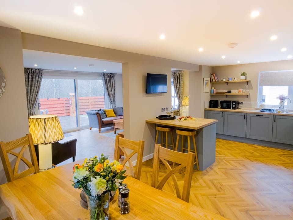 Get a feel for the wonderful open-plan layout of Kestrel Lodge in this wide-angle view. The light-filled space seamlessly connects the dining area, the comfortable lounge with patio doors to the garden, and the fully equipped kitchen. With warm herringbone flooring throughout, it is a sociable and family-friendly space that makes for a truly special self-catering holiday in Aviemore.