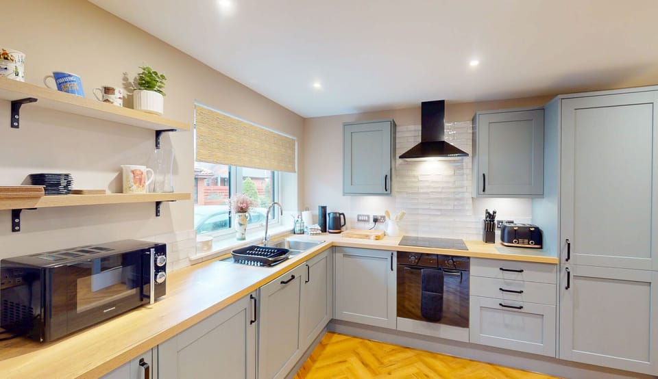 A close-up view of the well-equipped kitchen at Kestrel Lodge, showcasing the quality grey shaker-style units with wooden worktops, open shelving stocked with crockery, and integrated appliances. Everything the family needs for a comfortable self-catering stay in the heart of the Scottish Highlands is right at hand.