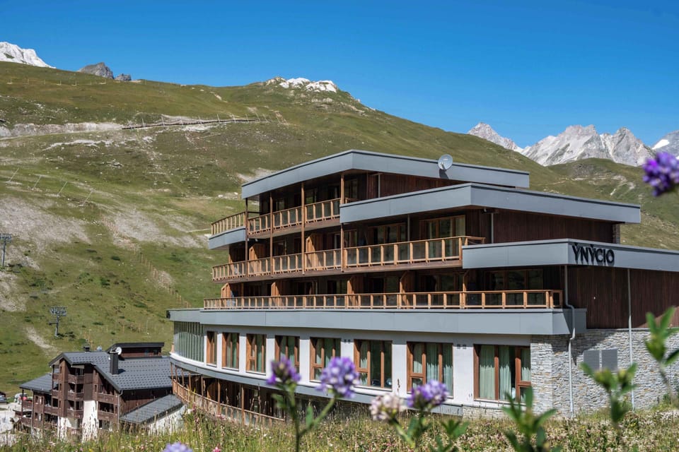 Wood-clad façade and stacked balconies overlooking the green slopes of Tignes Val Claret