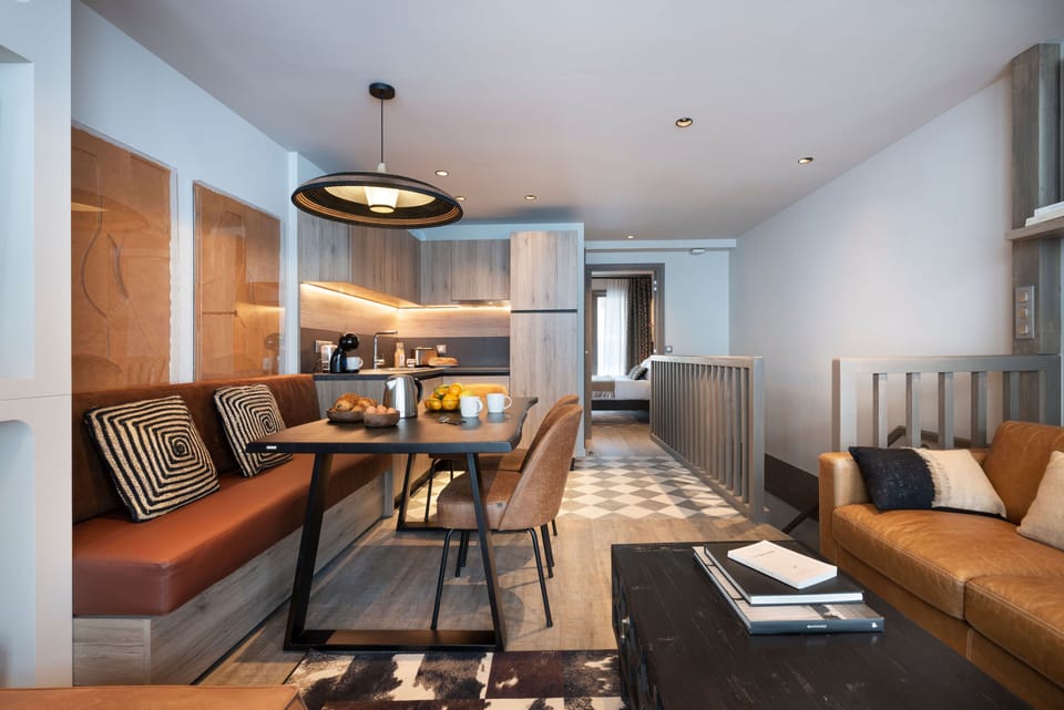 Open-plan living and dining area with a pendant-lit table, kitchenette, and geometric-patterned soft furnishings