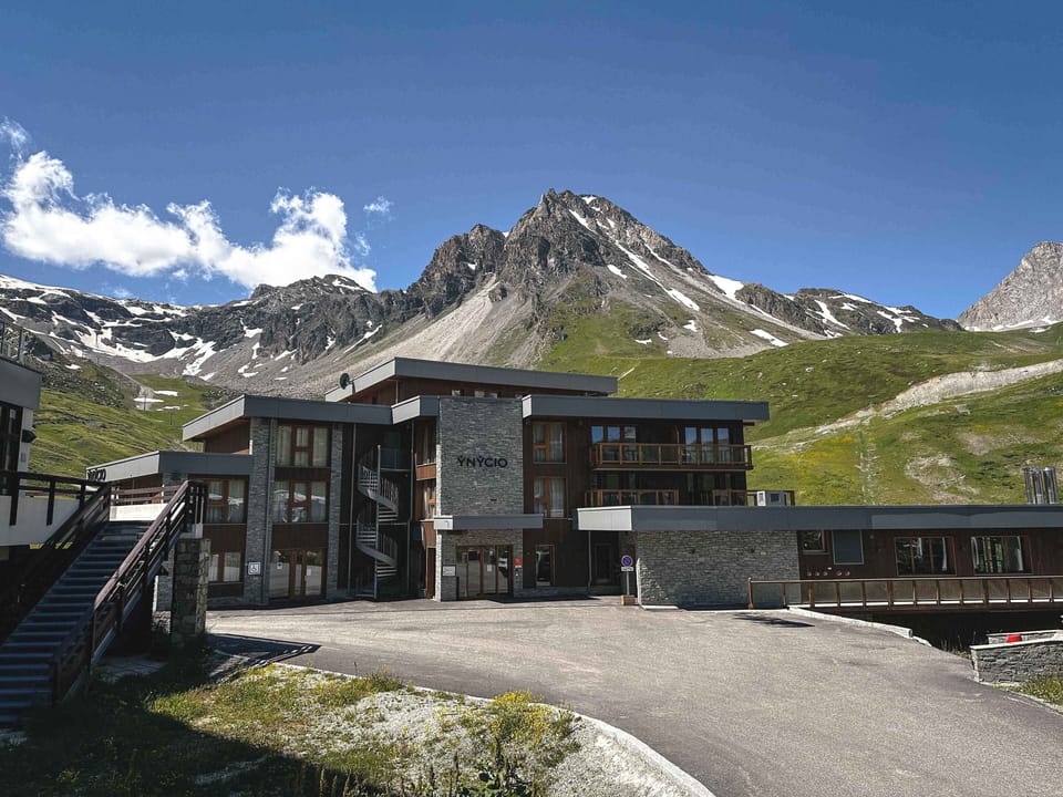 Four-storey alpine building set against the rocky peaks of the Espace Killy, with the Grande Motte visible in the distance
