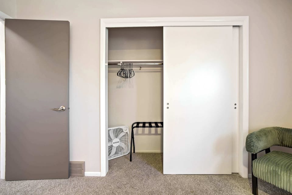 The primary bedroom closet offers a full sliding door setup with hanging space and room for luggage. A green accent chair sits just beside it, adding a touch of character to this comfortable and well-appointed room.
