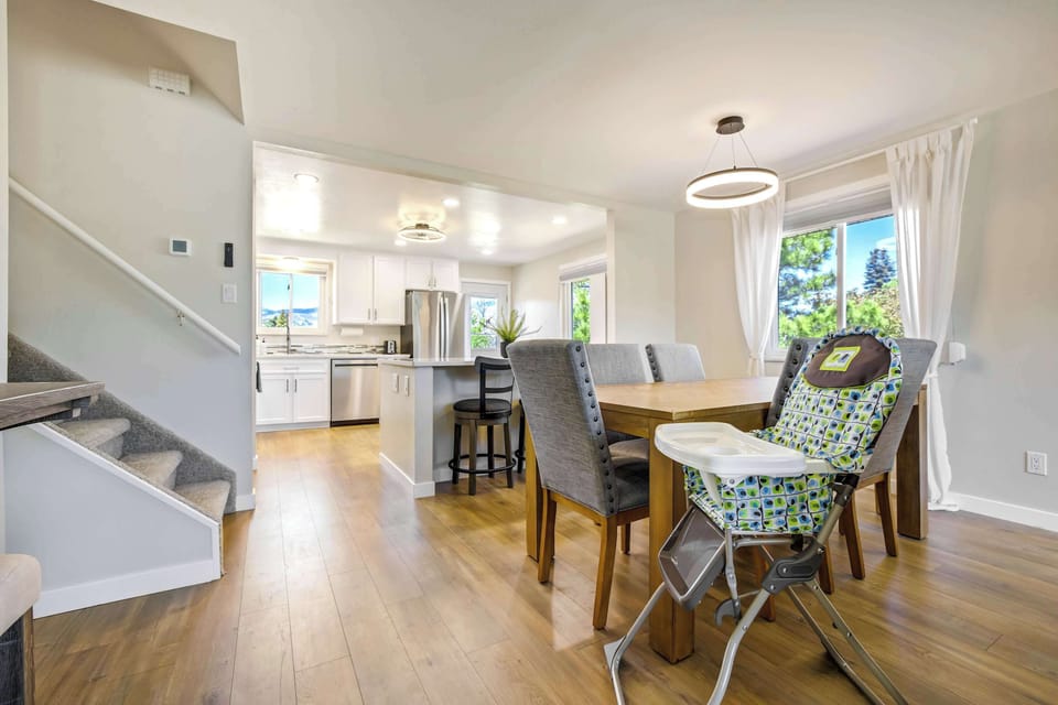 The open dining area flows naturally from the living room, with a patterned accent chair, pendant lighting, and a high chair ready for little ones. Views straight into the kitchen keep the connected layout easy for the whole group.