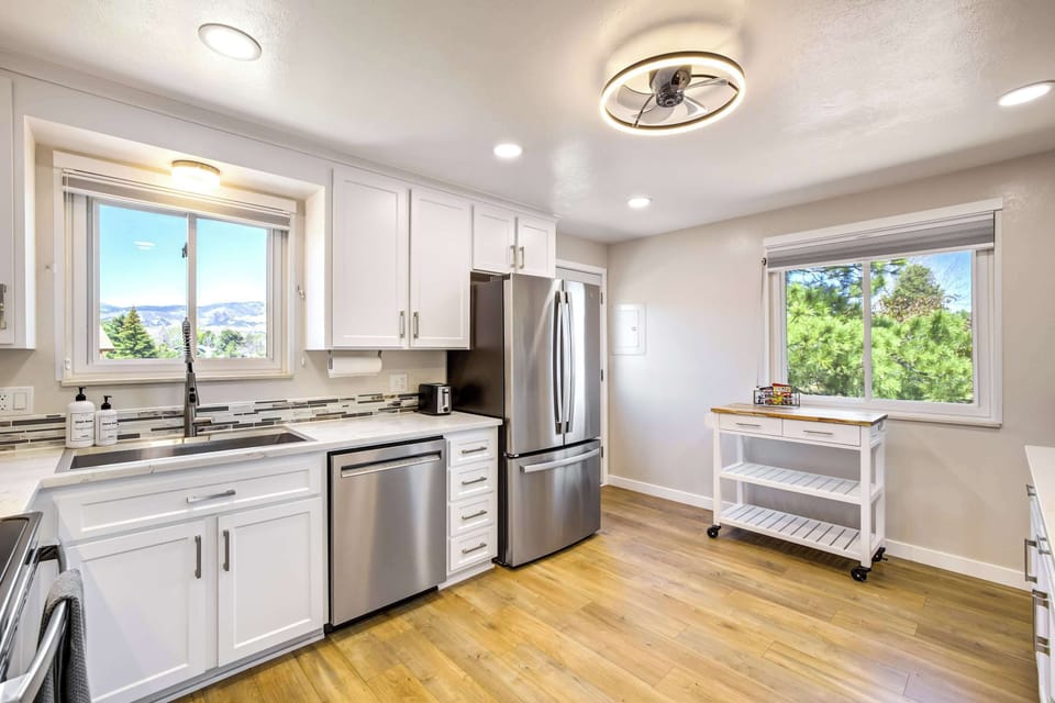A second angle reveals the full kitchen layout, with stainless refrigerator, stove, and ample counter space along both walls. Large windows on either side bring in natural light and frame views of the backyard and surrounding neighborhood.