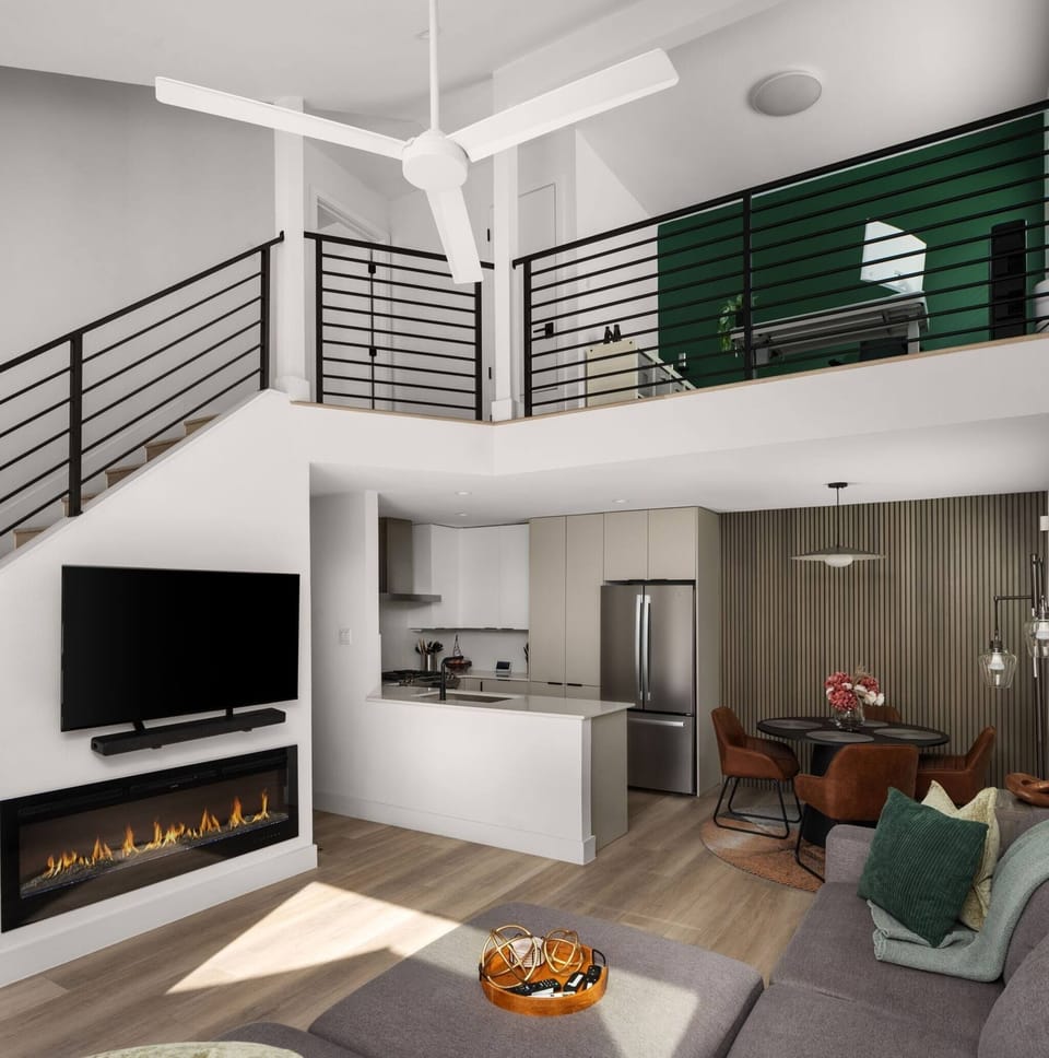 Stunning open-concept living space with soaring double-height ceilings, a sleek linear fireplace, large-screen TV, fully equipped kitchen, and loft above — an impressive and comfortable space to gather and unwind.