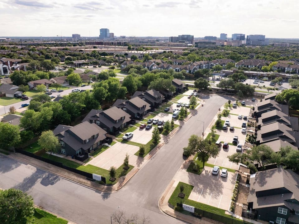 Sweeping aerial view of the property and surrounding community, with a city skyline visible in the distance — ideally situated close to urban conveniences while nestled within a tree-lined, well-connected neighborhood.