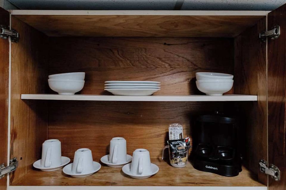 Kitchen cabinet in Isla Verde condo stocked with bowls, plates, coffee cups, and a coffee maker.