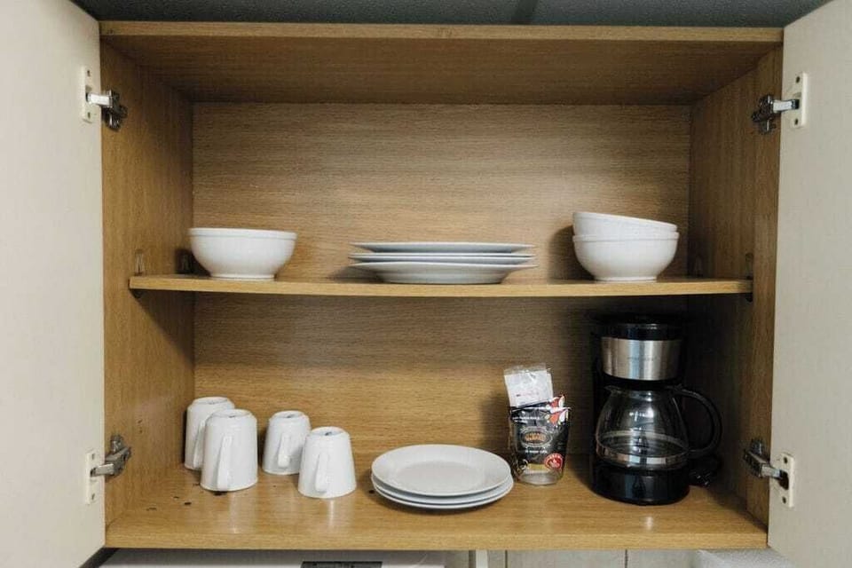 Open cabinet with plates, bowls, coffee mugs, and a drip coffee maker plus starter coffee, giving you everything needed for easy in‑studio meals.