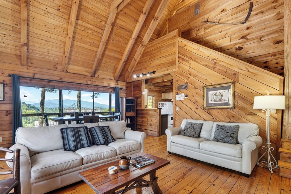 Warm cabin living room with a queen sleeper sofa, rustic wood accents, and big windows framing peaceful mountain views. (Elianah's Cabin)