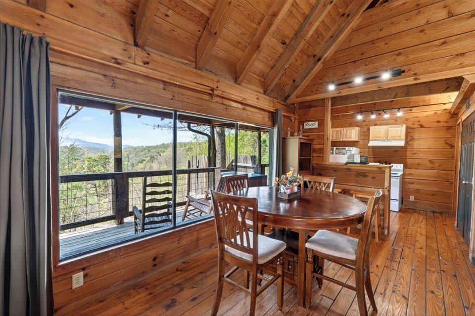 Cozy cabin dining nook with a round wooden table, warm natural light, and mountain views framed through the large window. (Isaiah's Cabin)