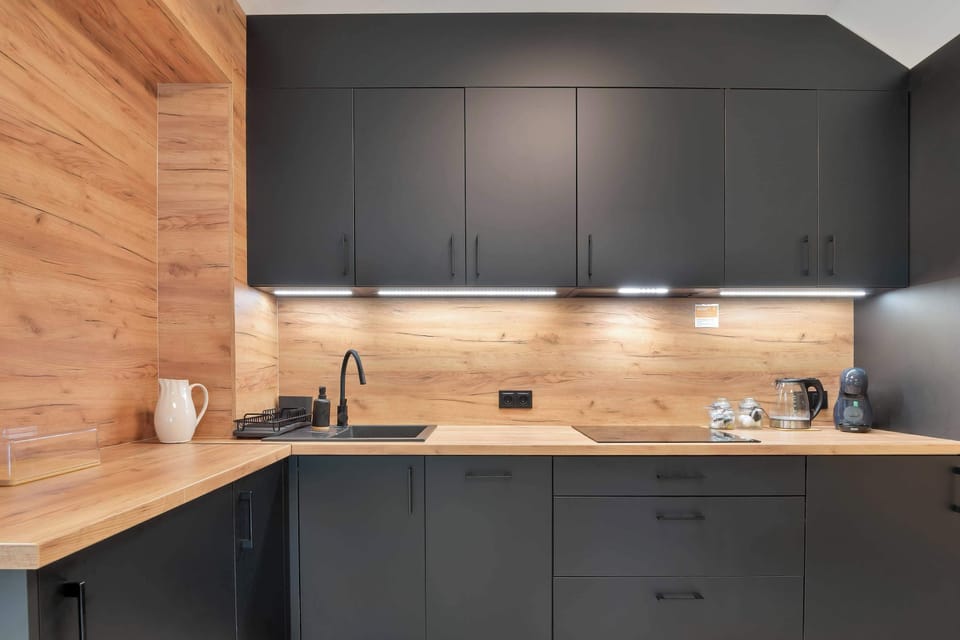 A modern kitchenette with black cabinets, wooden walls, and built-in appliances.