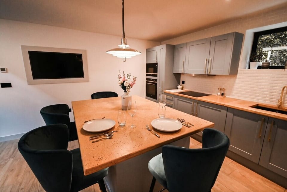 Cook and gather in a stylish kitchen with stone island, velvet chairs, and a wall TV.