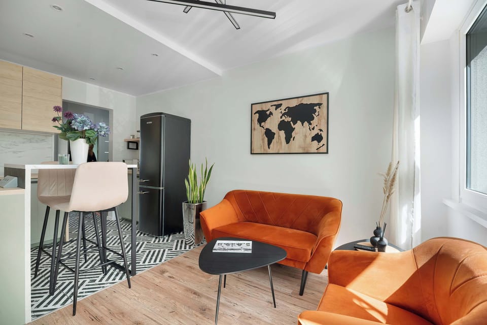 The open-plan layout connects the kitchen island with the living room, featuring a trendy orange sofa and wall decorations.