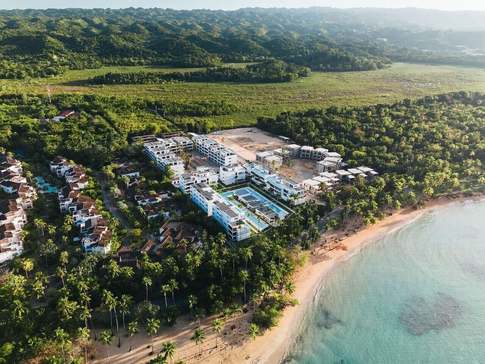 Aerial view of Residencial Sol de Arena: modern beachfront condos with pools, palm trees, and ocean in Las Terrenas.