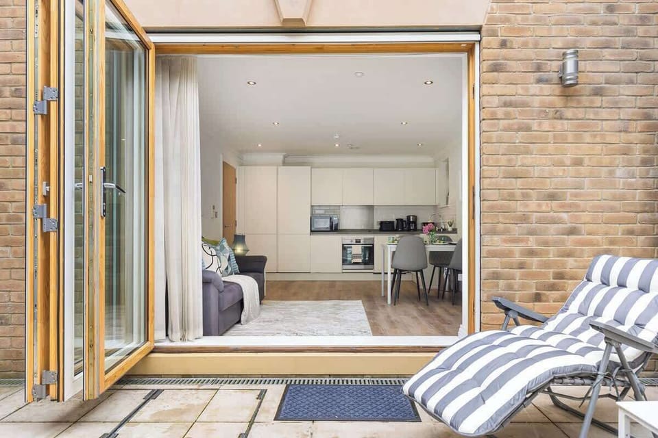 Step outside into this private paved patio area, featuring a comfortable striped lounge chair and wide bi-fold glass doors that open directly into the open-plan living, dining, and kitchen space.