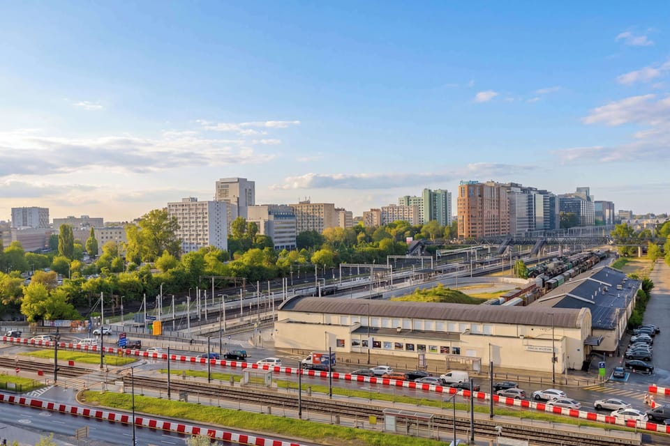 An elevated panoramic view captures an urban landscape featuring roads, greenery, and buildings under a bright sky. The perspective showcases the vibrant city infrastructure from a high vantage point.
