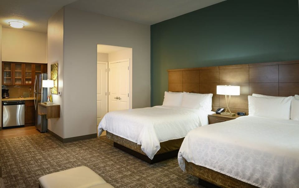 This view shows two queen beds next to a compact kitchen area with a full-size refrigerator and microwave.