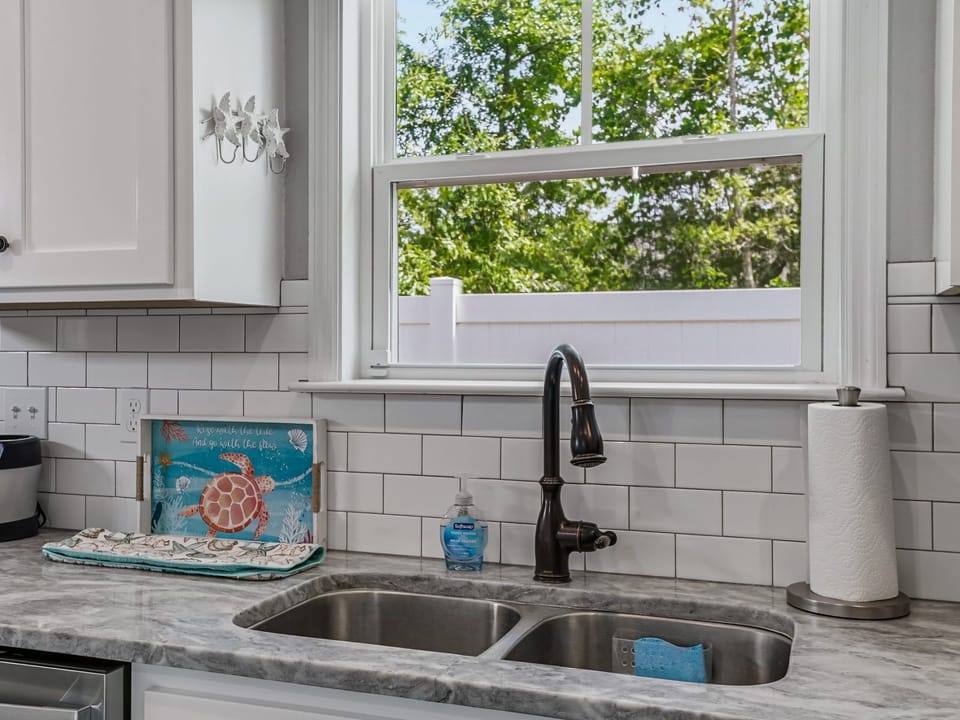 Kitchen sink with subway tile backsplash, marble counter, coastal decor, and a window overlooking the yard