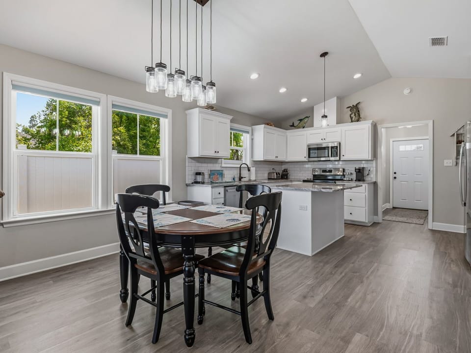 Bright kitchen with dining table for four, white cabinetry, stainless appliances, and green views outside