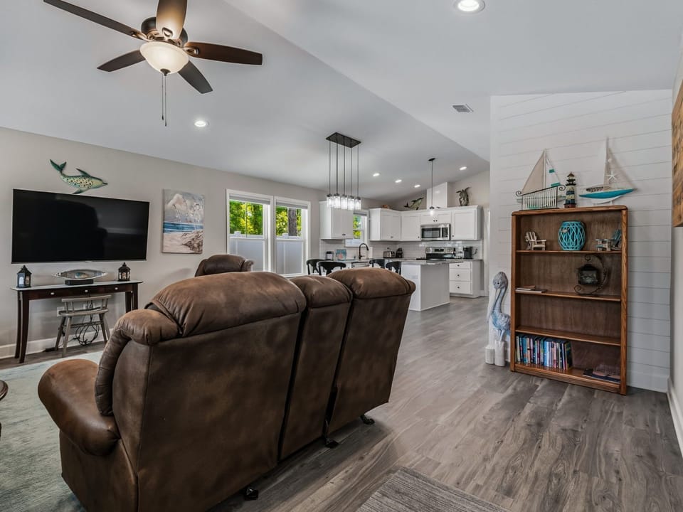 Open-plan living and dining area with two brown recliners, wall TV, round table, and white kitchen visible beyond