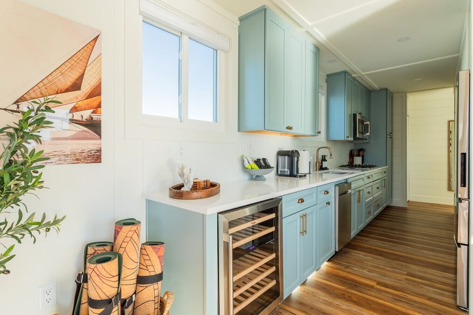 The galley kitchen with custom blue-gray cabinetry, quartz counters, brass hardware, a built-in wine fridge, and a Nespresso maker, running the full length of the space with warm wood floors throughout.