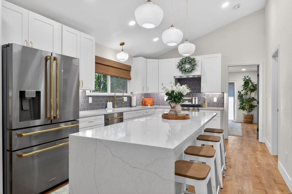 Step into a stunning chef`s kitchen with a massive waterfall quartz island, premium ZLINE appliances with brass accents, custom picket backsplash, and designer pendant lighting. Vaulted ceilings and white shaker cabinets create pure luxury living
