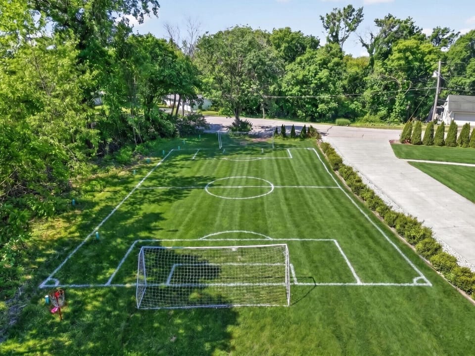 Expansive backyard with plenty of open green space for sports and play, featuring two full-size soccer goals and a disc golf basket. Lush grass framed by mature trees—perfect for pickup games, family matches, or just letting the kids run