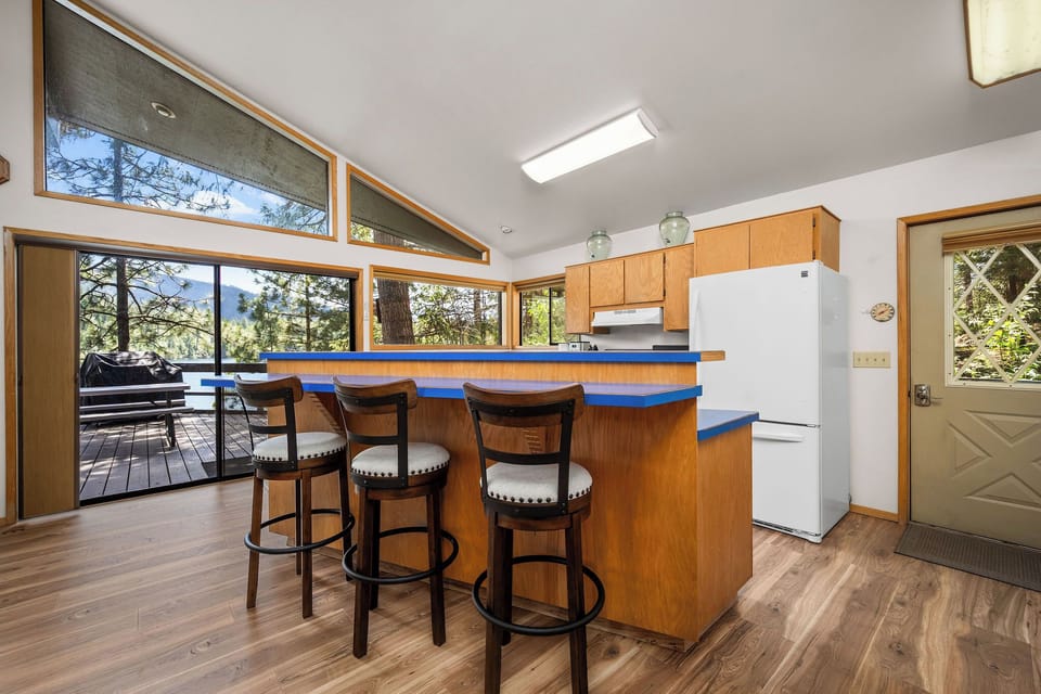 Gather at the vibrant blue breakfast bar, where forest views frame your morning coffee. Sunlight streams through vaulted windows, connecting your kitchen to treetops and mountain air beyond.