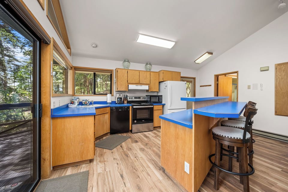 Cook and gather around the vibrant blue counters as sunlight pours through skylights and windows framing forest views—your mountain retreat kitchen awaits.