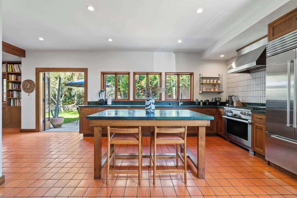 Kitchen — Oak Cabinets, Dark Green Soapstone Island with 2 Bar Stools, Terracotta Tile Floor, Professional Stainless Range, Stainless Hood, White Grid Tile Backsplash, Built-In Refrigerator & Garden-View Windows