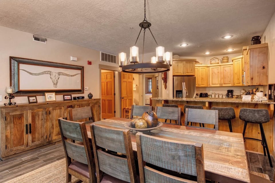 This spacious dining area features rustic charm, a central chandelier, and open sightlines to the kitchen and great room.