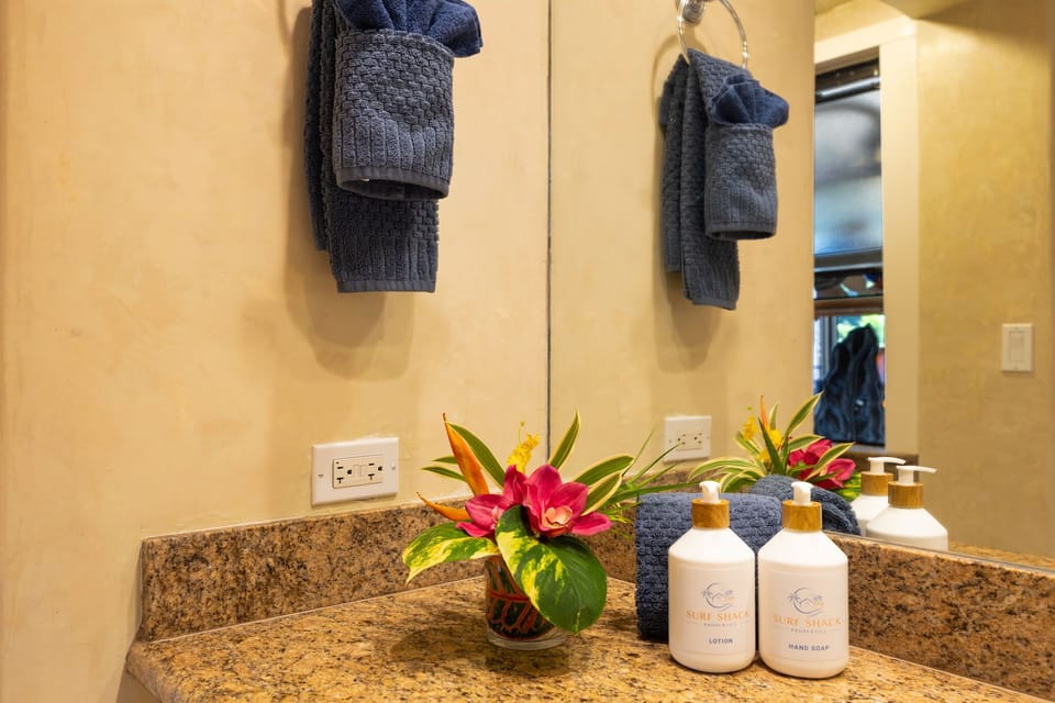  Close-up of the bathroom vanity featuring granite countertops, fresh hand towels, a beautiful tropical floral arrangement, and provided hand soap and lotion for your convenience 