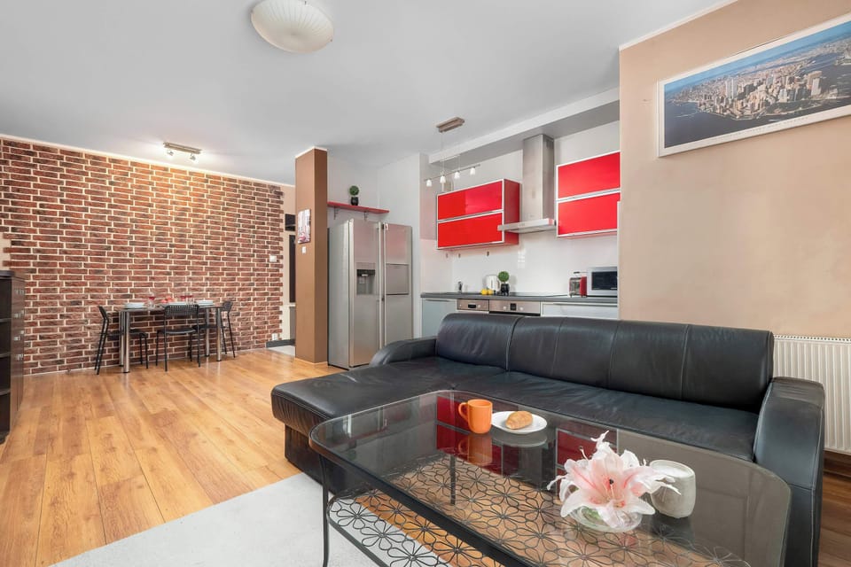 Bright living room with a black sofa, glass coffee table, and modern red kitchen cabinets.