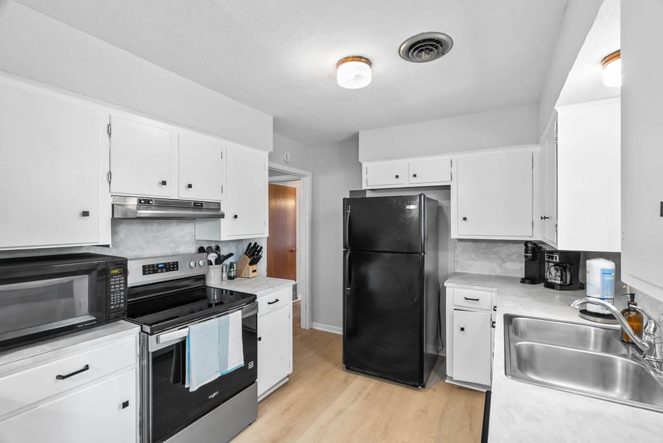 Modern kitchen equipped with sleek white cabinetry, updated countertops, and a bold black refrigerator.