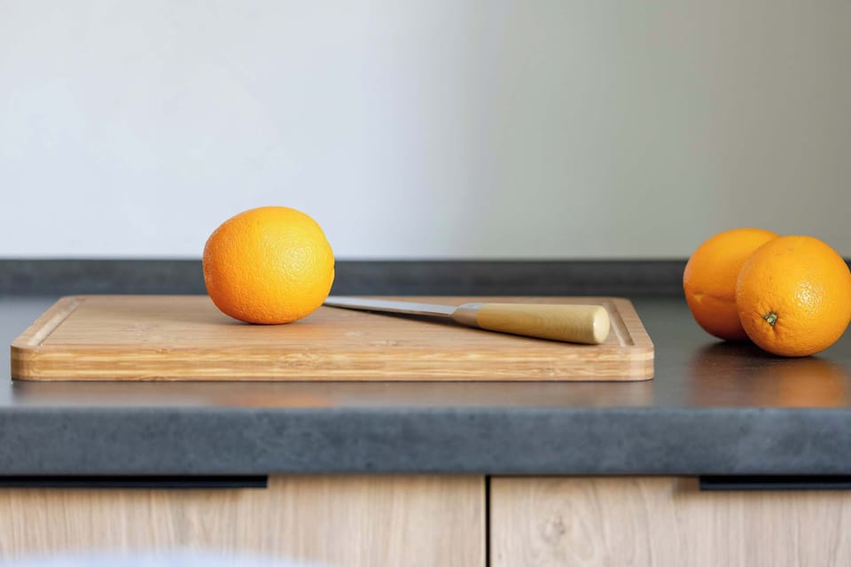 A close-up shot focuses on a wooden cutting board with a knife and fresh oranges on a clean kitchen counter. This detail emphasizes the home's readiness for daily living and food preparation.