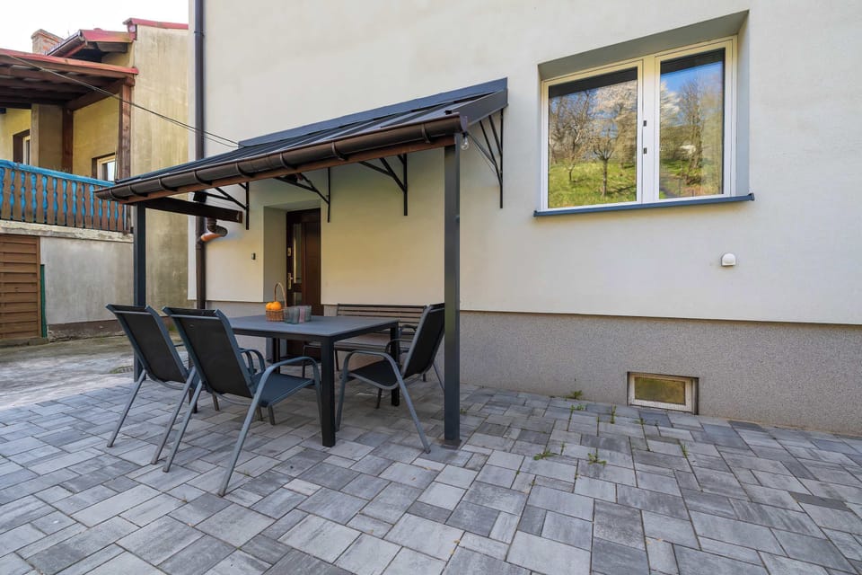 An outdoor patio area is paved with grey stones and offers a black dining set under a protective awning. This space provides a private spot for al fresco dining right next to the house wall.
