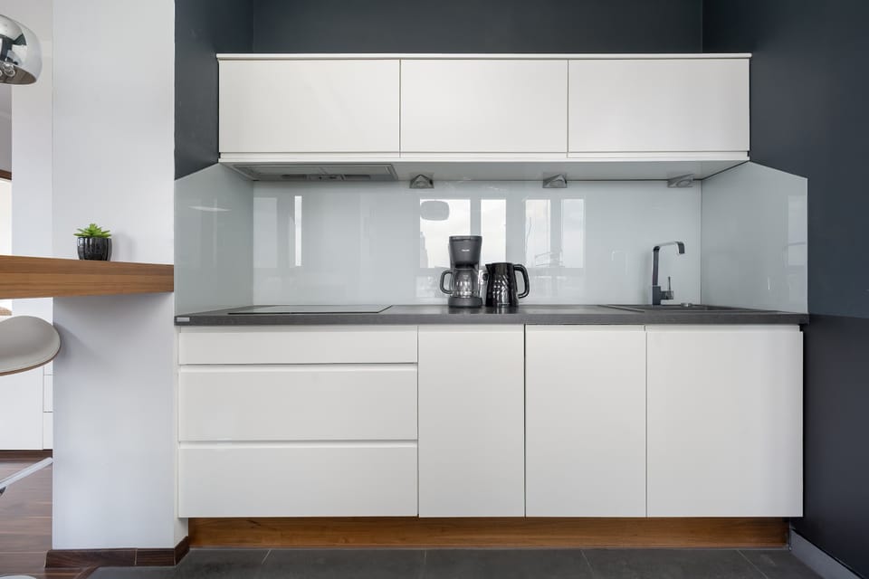 A sleek, modern kitchen displays clean white cabinetry and a dark countertop for a sharp, contemporary look. The minimalist backsplash and integrated appliances emphasize the functional yet stylish design.