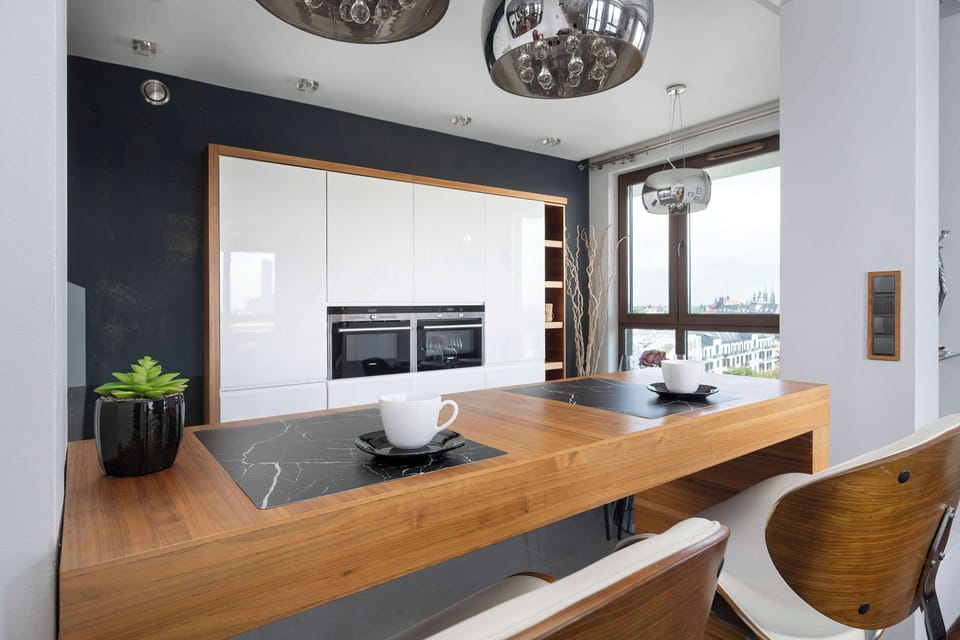 A detailed shot of the breakfast bar captures the contrast between the warm wood surface and the sleek white kitchen units. Modern pendant lighting and a small potted plant add decorative flair to the workspace.