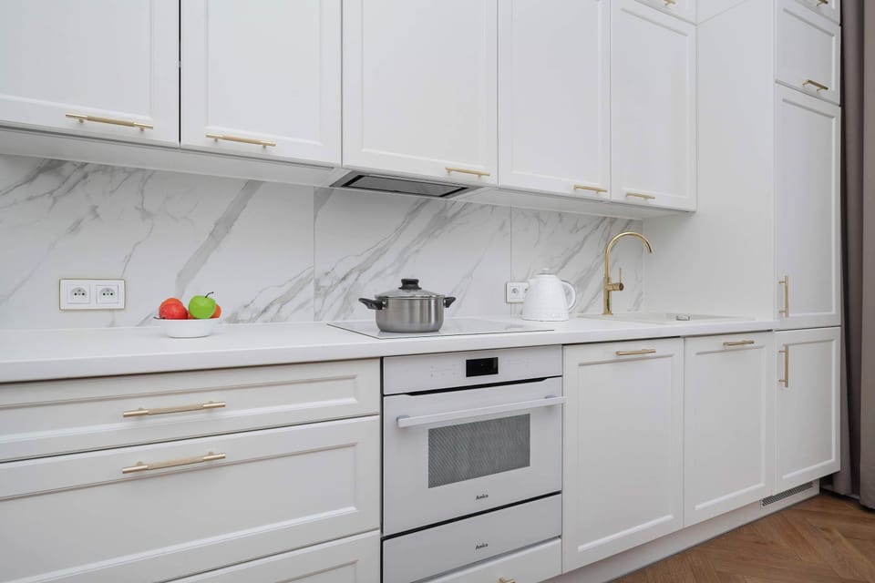 A sleek white kitchen with marble-style backsplash tiles and built-in appliances.