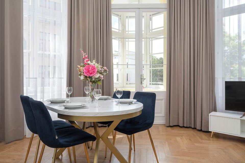 A dining corner with dark blue chairs positioned beside large windows and flowing curtains.