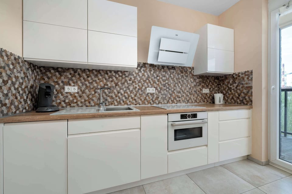 A modern kitchen with a stylish backsplash and built-in appliances. The space is fully equipped for cooking at home.