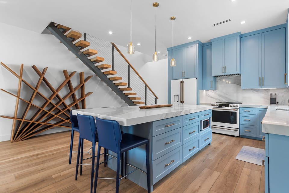 Spacious kitchen featuring oversized island, designer lighting, and a striking floating staircase centerpiece