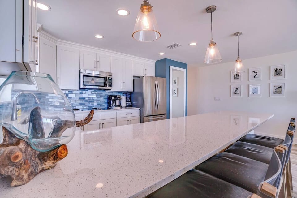 Picture yourself cooking in this bright, modern kitchen with gleaming countertops, stainless appliances, and coastal touches that make every meal feel like a vacation moment.