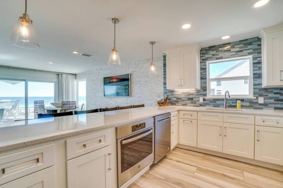 Picture yourself preparing meals in this bright coastal kitchen with ocean views just beyond the dining area, modern appliances, and stylish tile details throughout your stay.
