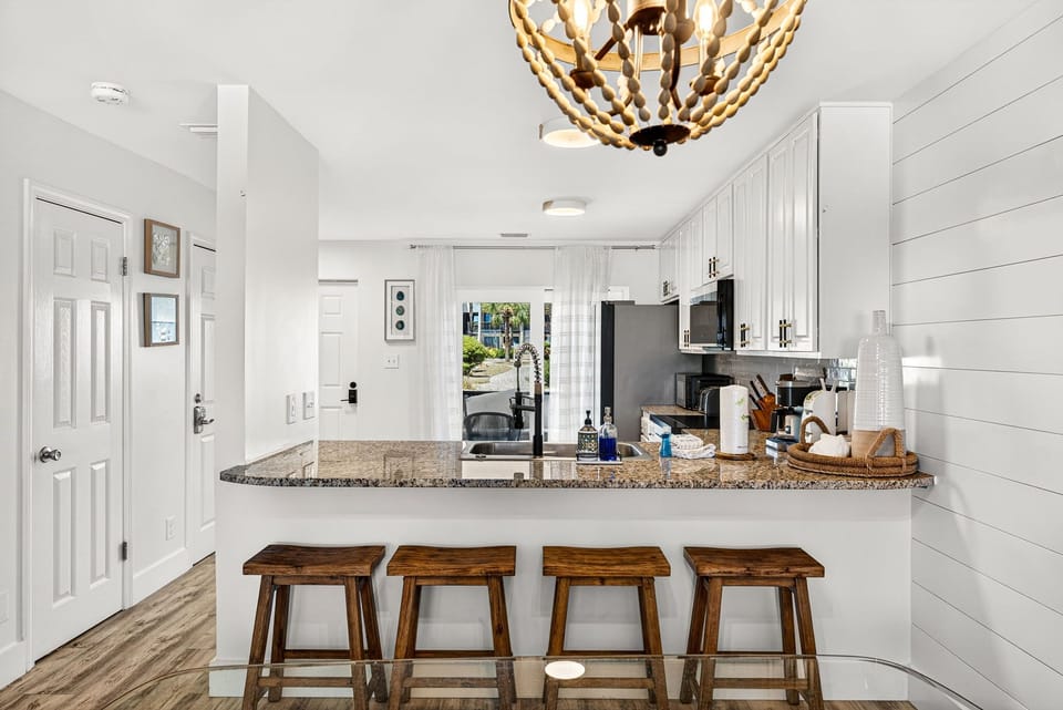 Gather around your beautiful granite-topped breakfast bar and enjoy morning coffee under charming coastal-inspired lighting. The open kitchen flows seamlessly to bright outdoor views beyond.