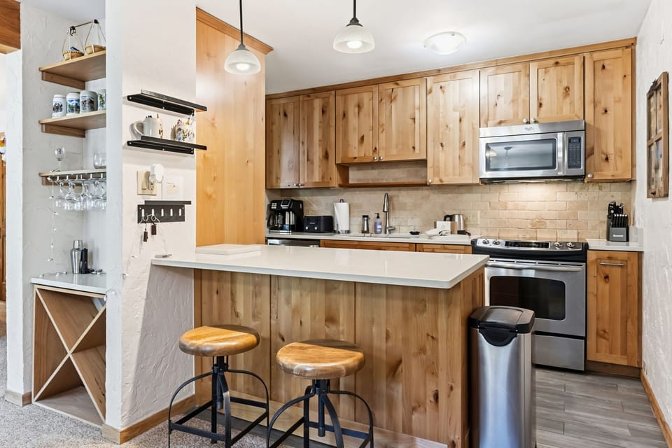 Picture yourself preparing your favorite meal in this warm, fully-equipped kitchen with a functional island, modern appliances, and charming rustic cabinetry illuminated by inviting pendant lighting.