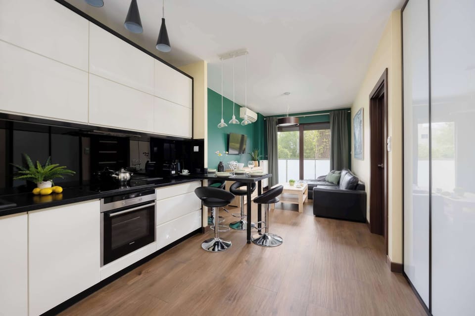 An open-plan kitchen extending into a hallway with glossy white cabinetry and wood flooring. Decorative shelves and hanging lights create a polished interior design.