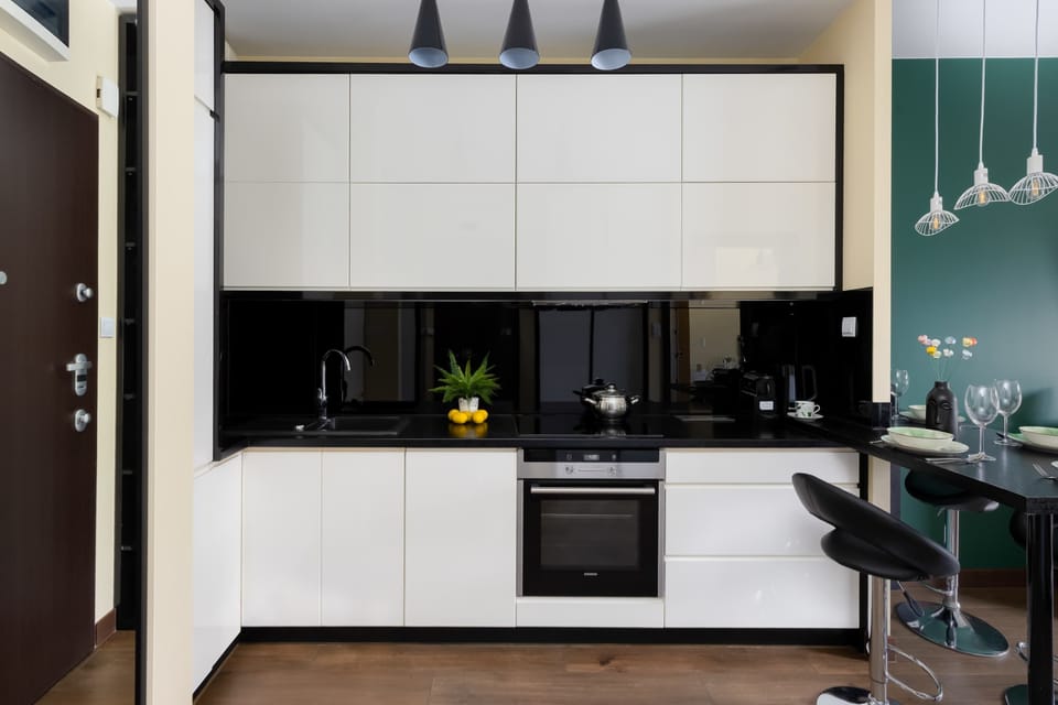 A stylish kitchenette with built-in appliances, glossy cabinets, and a small dining corner. Black surfaces and teal wall accents create a modern urban look.